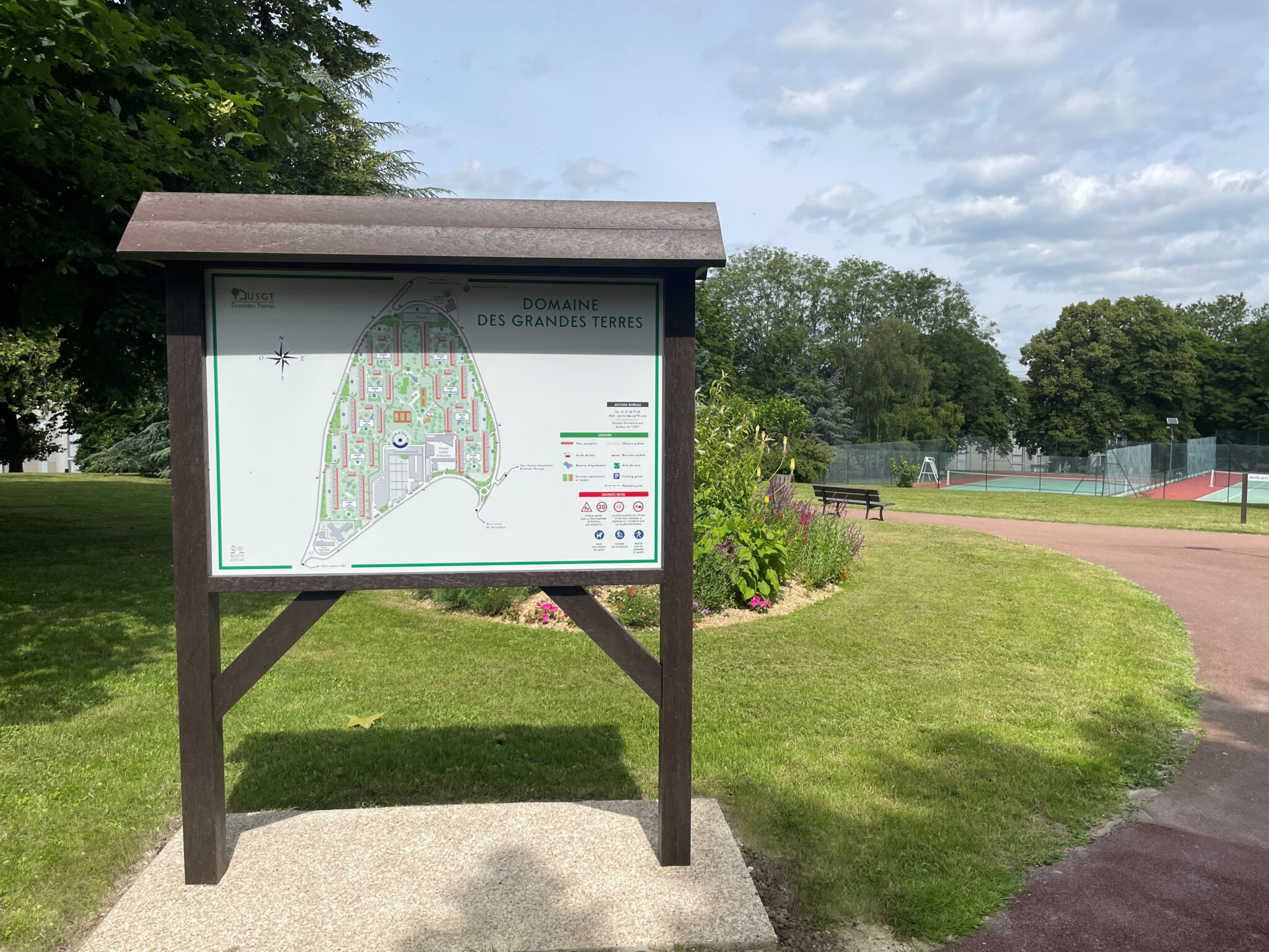Panneau d'information dans parc avec carte et tennis.